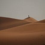 a lone person standing on top of a sand dune