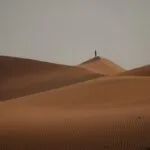 a lone person standing on top of a sand dune