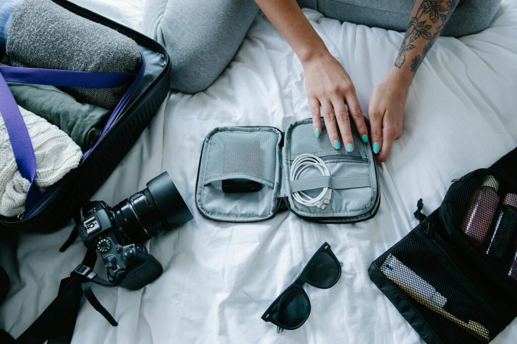 Woman with tattoos packs electronics, camera, and sunglasses in a suitcase on a bed.Morocco Dress Code