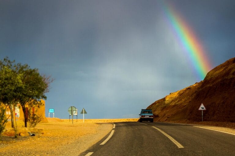 A vibrant rainbow arches over a road near Aït Ben Haddou, Morocco, capturing a stunning desert landscape.