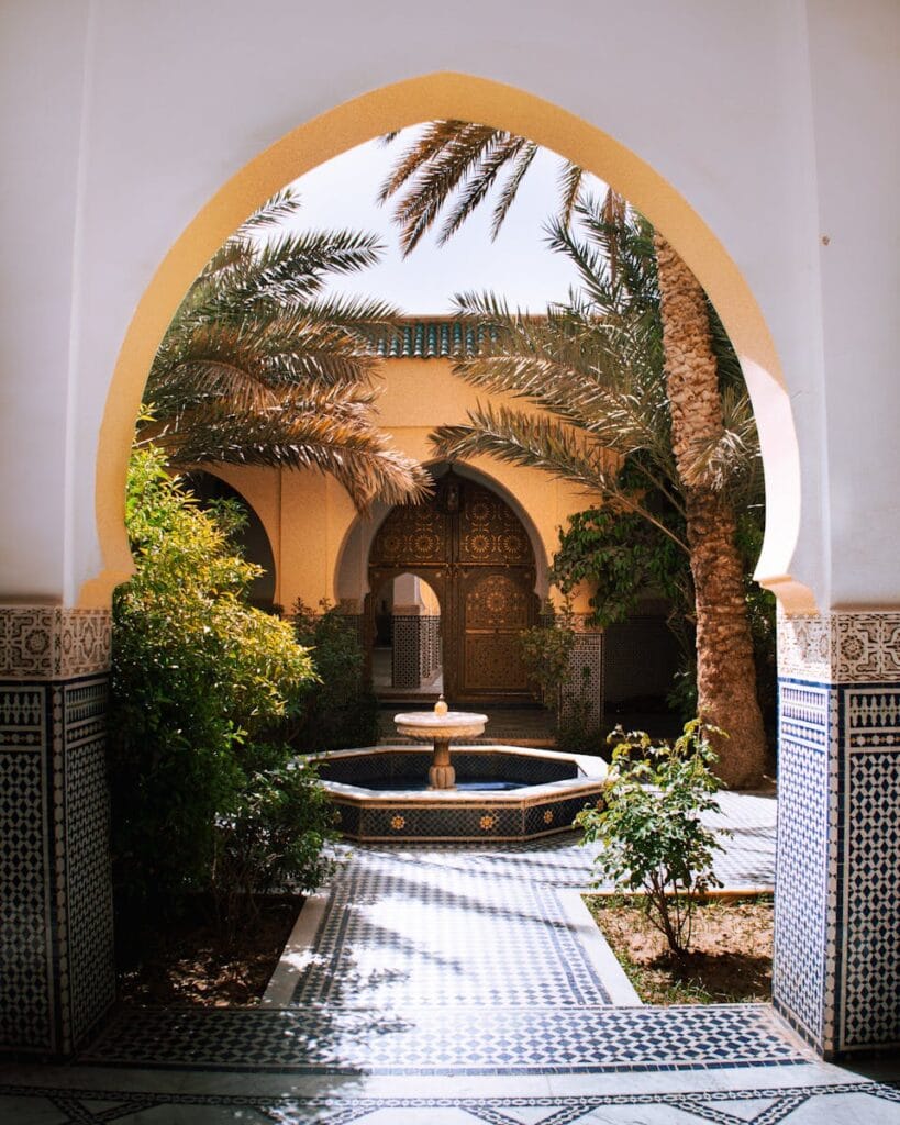 Serene Moroccan courtyard featuring a traditional fountain, palm trees, and ornate archways.Rissani Marokko