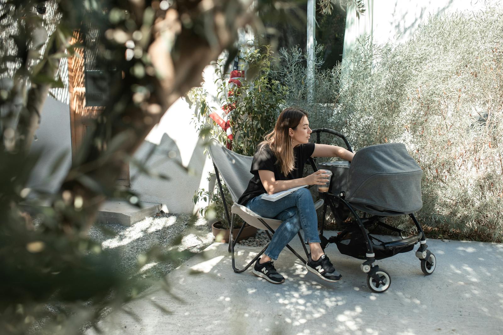 A mother sitting outdoors enjoying a sunny day with her baby in a stroller.