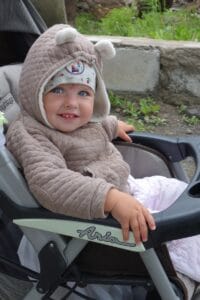 A smiling baby in a stroller wearing a hooded jacket.