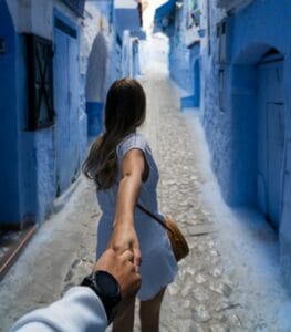 woman holding man's hand while walking on alley.chefchaouen