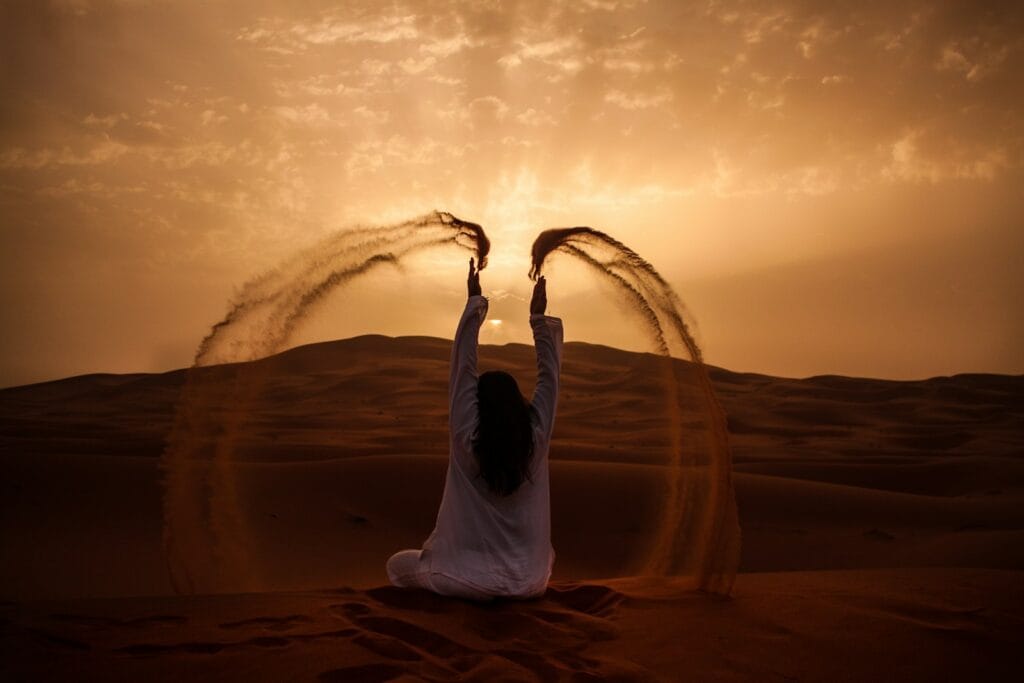 woman sitting on desert while playing sand during golden hour,Merzouga Weather in December