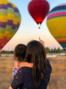 woman carrying toddler point at hot air balloon.Morocco with Family