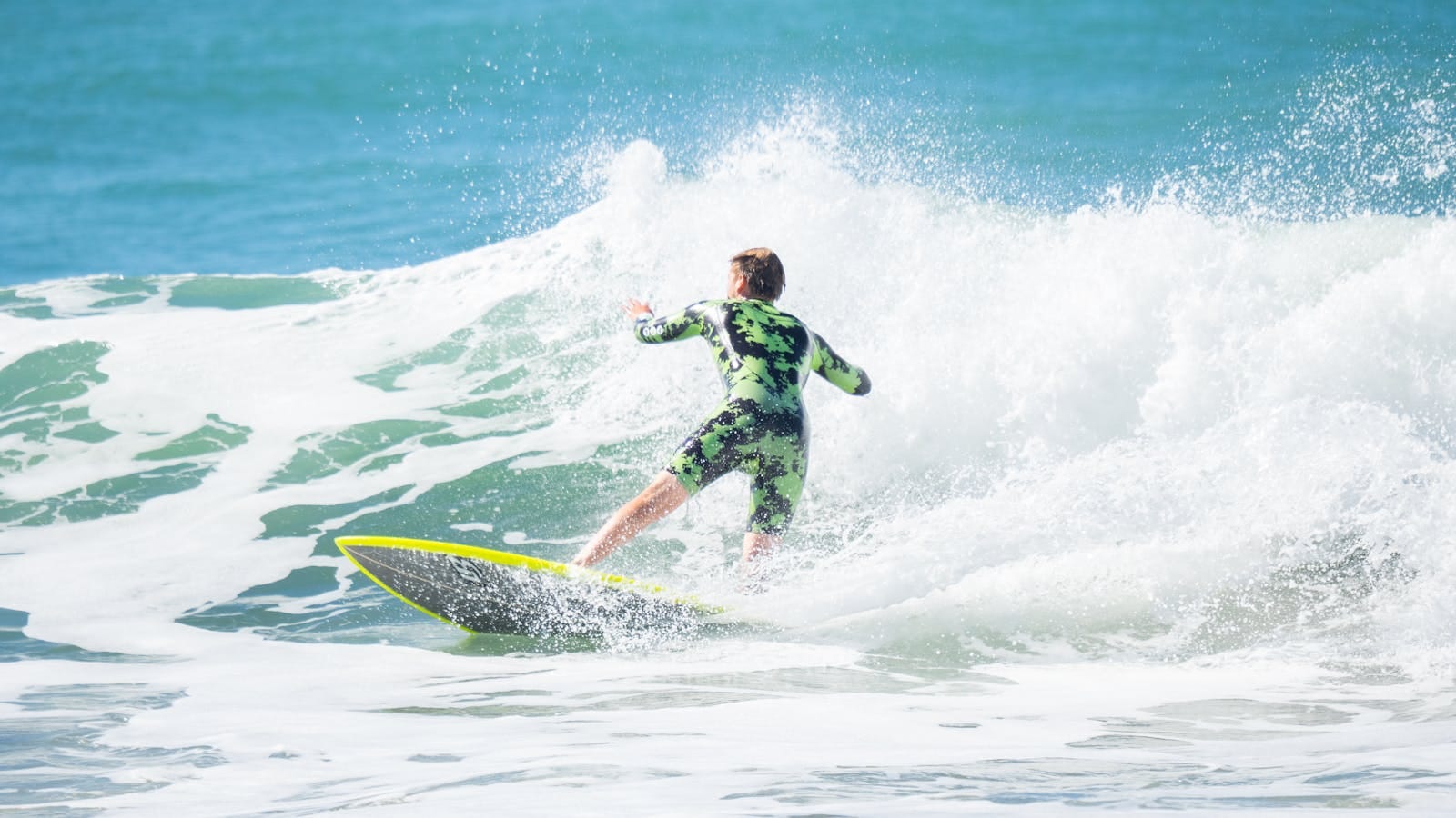 A surfer in a wetsuit rides a wave on a sunny day at the beach. Action-packed and vibrant.Family Surfing Vacations Morocco