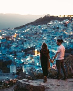 A romantic couple holding hands with a view of Chefchaouen, Morocco at twilight.disrespectful in Morocco