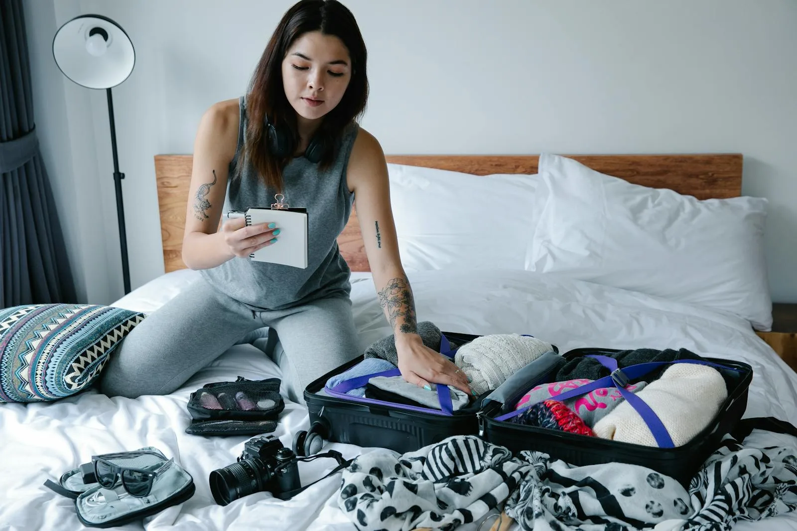 Woman sitting on bed packing a suitcase and taking notes for her travel plan.packing list