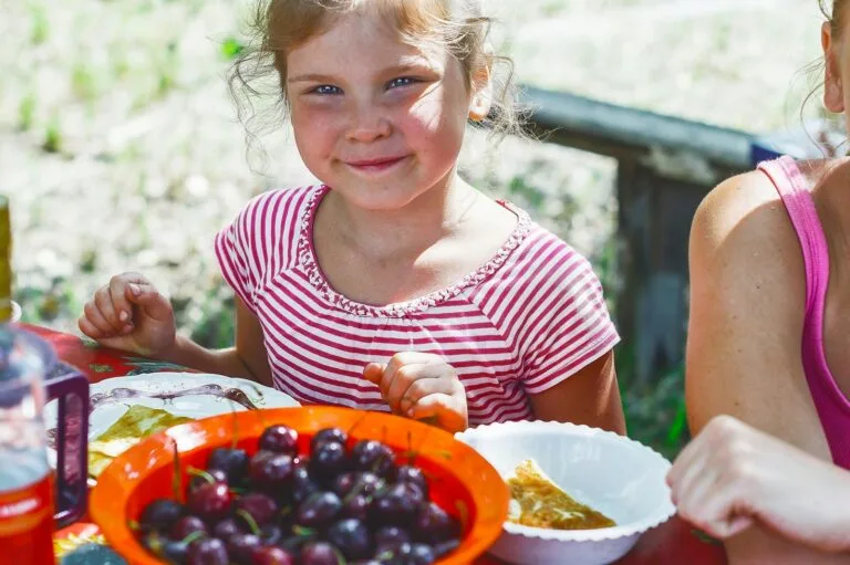 girl in red and white striped shirt holding white ceramic bowl with red and black fruits,moroccan food