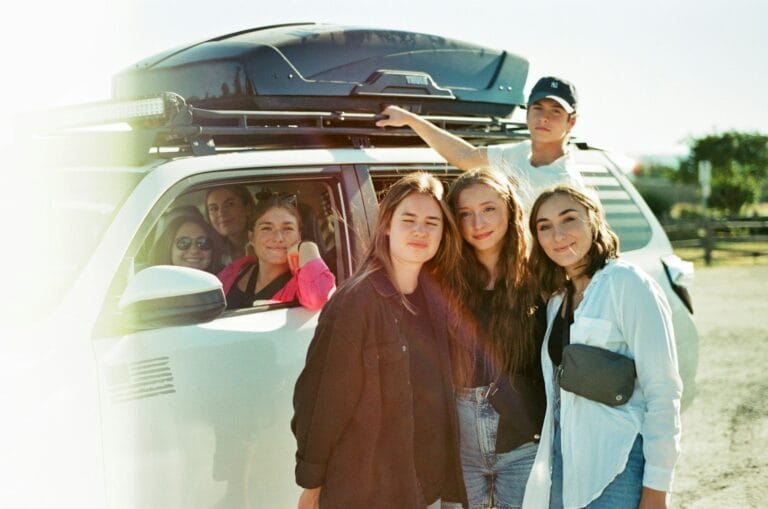 a group of people standing in front of a van.Teenagers