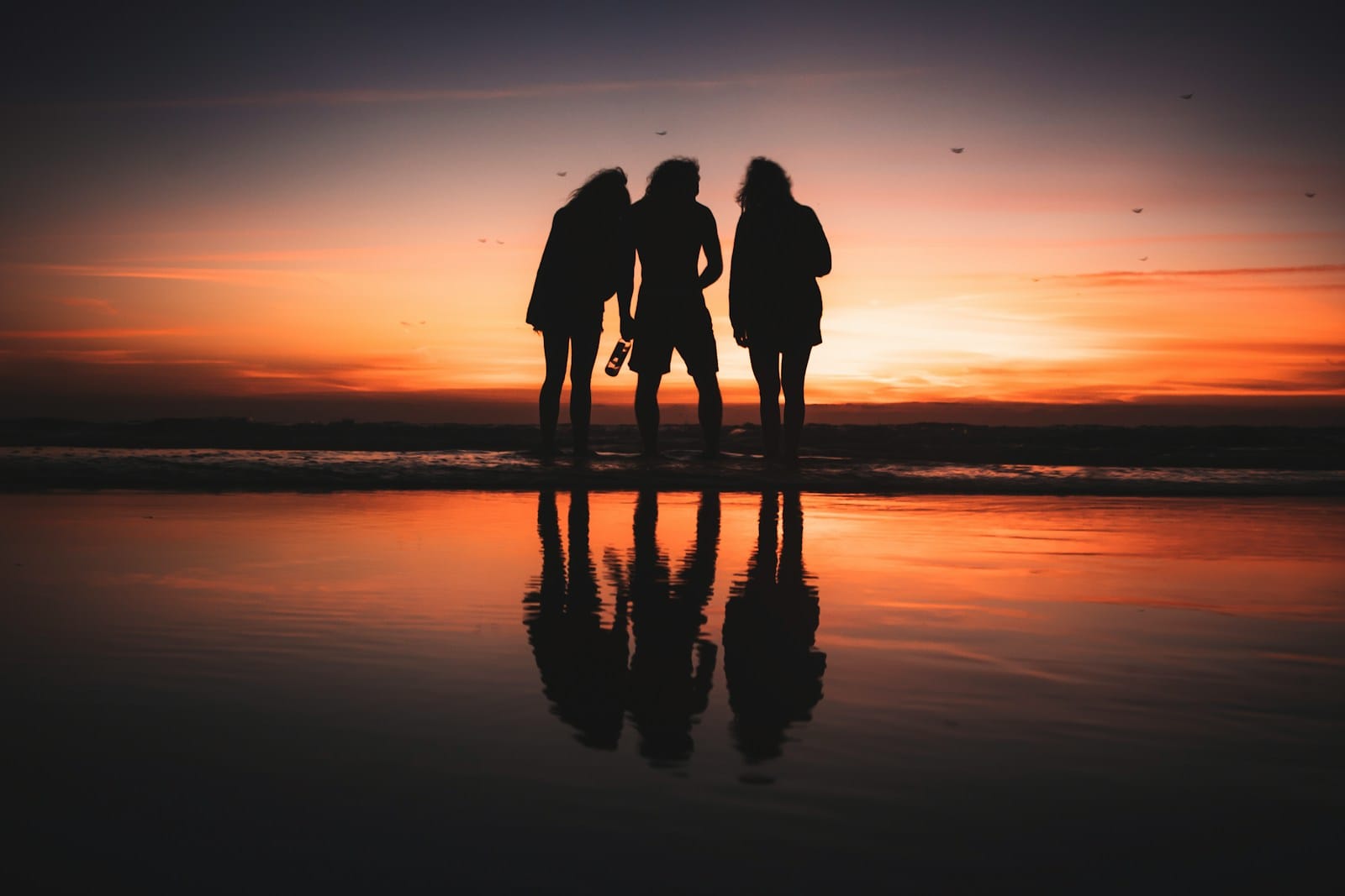 a group of people standing on a beach at sunset.Teenagers