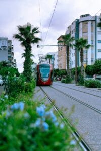 A red train traveling down train tracks next to tall buildings.Marrakech or Casablanca