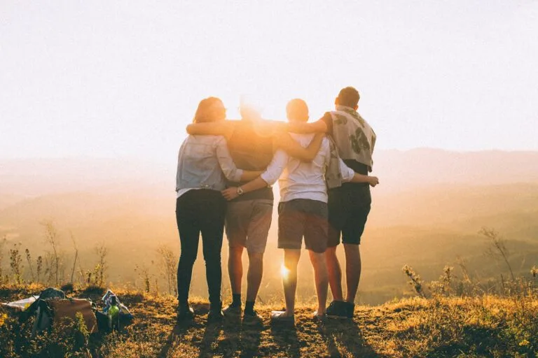 four person hands wrap around shoulders while looking at sunset.Morocco with Family