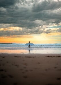 A serene view of a surfer walking along the beach with a surfboard at sunset in Essaouira, Morocco.Agadir or Essaouira