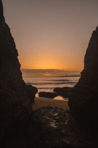 the sun is setting over the ocean and rocks