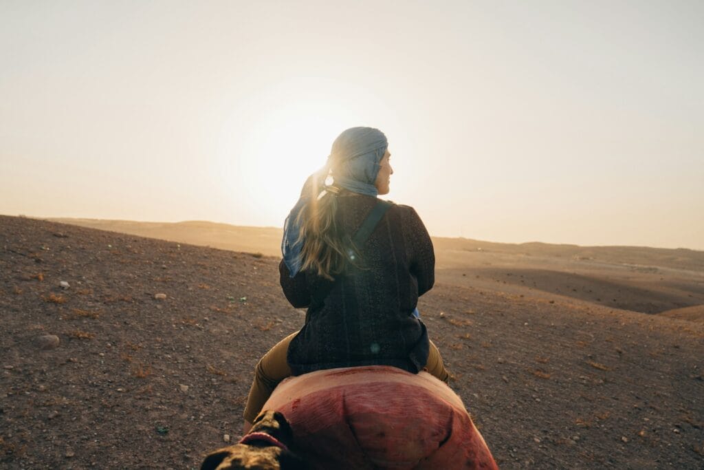 Woman riding camel in desert at sunset