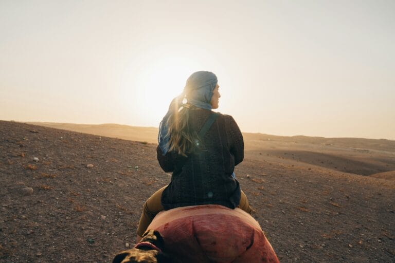 Woman riding camel in desert at sunset