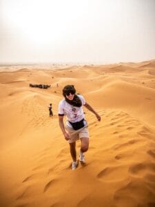 a man walking across a sandy field.Merzouga From Marrakech