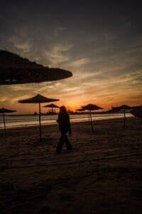 A striking silhouette of a woman walking along a beach in Morocco during a vibrant sunset.Marokko Kaart