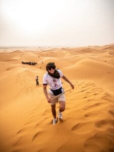 a man walking across a sandy field.Why is Erg Chebbi Famous