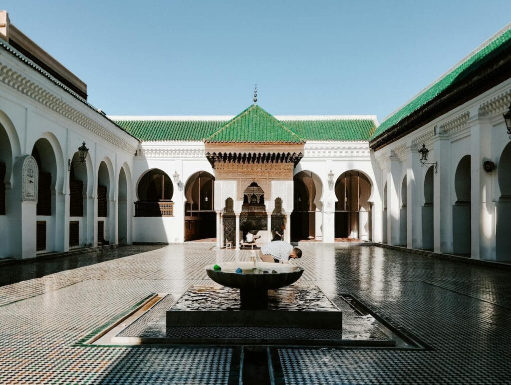 A view of the historic Al Quaraouiyine Mosque courtyard in Fes, Morocco with traditional architecture and ornate fountain.Is Morocco Expensive