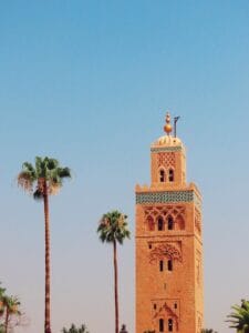 Iconic Koutoubia Mosque tower with palm trees in Marrakech against a clear blue sky.