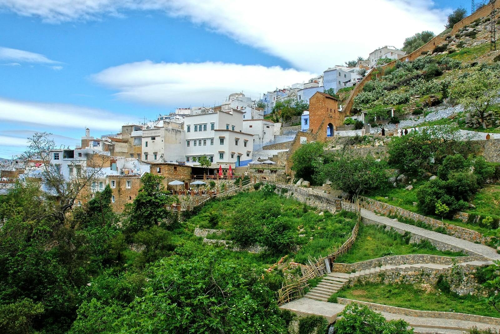 Captivating hillside view of Chefchaouen's unique architecture amid lush greenery and blue skies.berber village Morocco