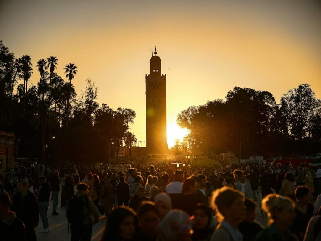 A bustling crowd gathers under the iconic Koutoubia Mosque tower at sunset in Marrakesh, Morocco.best time of year to visit Morocco