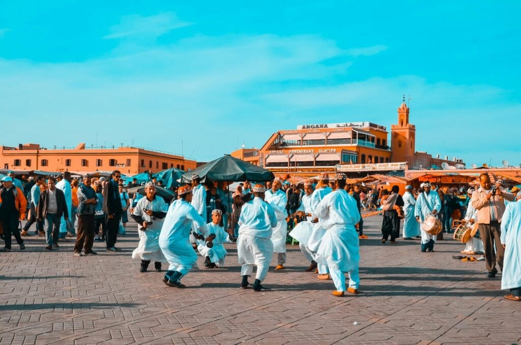 crowd of people walking near road beside buildings under blue and white sky during daytime