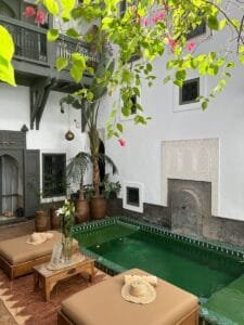 Charming Moroccan courtyard featuring a green pool, lush plants, and traditional architectural accents.what are riads in morocco