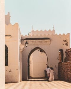 A couple strolls through a picturesque alley in Asilah, Morocco, under a clear sky.What to do in Asilah with kids?