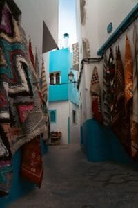 Vibrant Moroccan alleyway in Asilah with hanging carpets and blue walls.Is Asilah Worth Visiting for Families