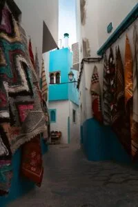 Vibrant Moroccan alleyway in Asilah with hanging carpets and blue walls.Is Asilah Worth Visiting for Families