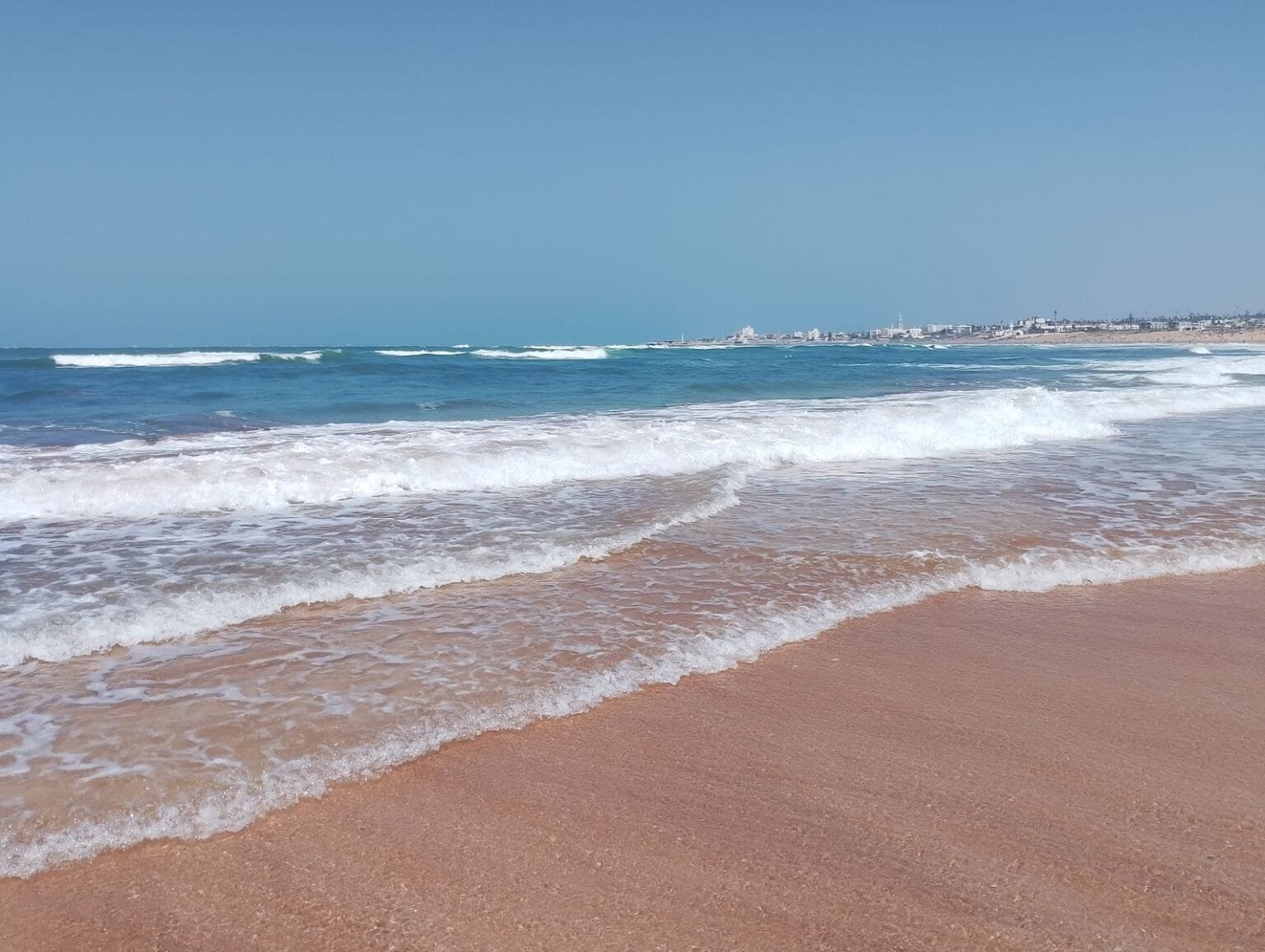 Captivating view of waves rolling onto a sandy beach under a clear blue sky.