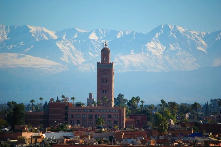 The Koutoubia Mosque minaret rising above Marrakesh with snow-capped Atlas Mountains in the background.morocco fez or marrakech