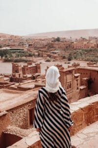Woman in a striped dress and headscarf admiring Aït Benhaddou's desert architecture..Tijdsverschil Marokko België