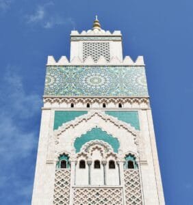 A striking vertical shot of the Hassan II Mosque's intricate minaret against a clear blue sky..Tijdsverschil Marokko België