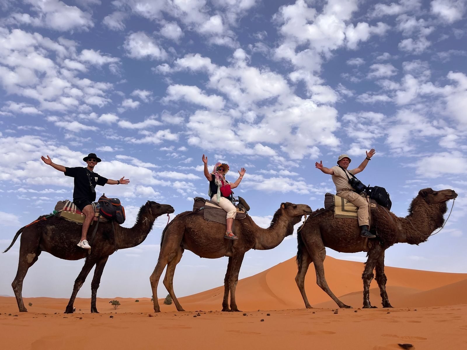 Three tourists riding camels in the Sahara Desert under a bright blue sky.Morocco With Kids