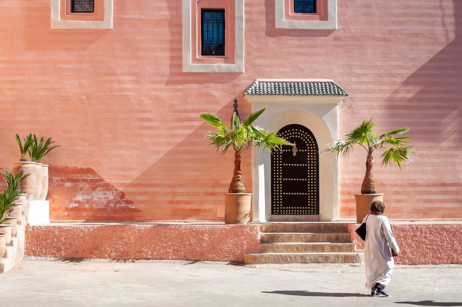 Back view of unrecognizable Muslim woman in traditional dress and headscarf walking in town near typical residential house on sunny day in Marrakesh,Language in Morocco