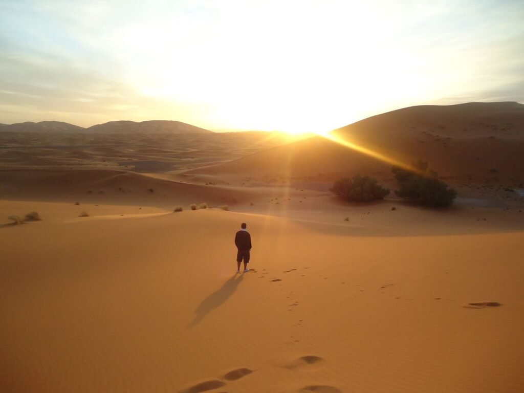 Silhouette of a man walking along sand dunes during a sunrise in the Sahara Desert.Tip in Morocco