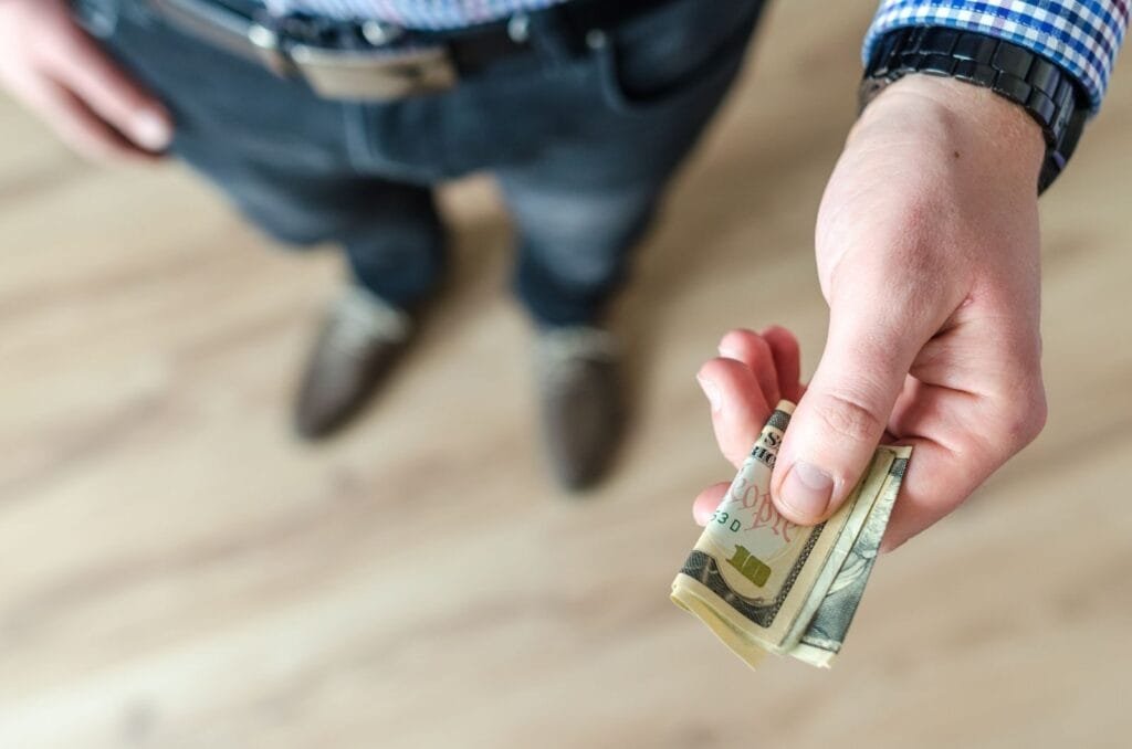 A close-up of a man's hand holding rolled US dollar bills, offering cash.Tip in Morocco