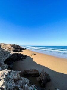 a sandy beach with rocks and water on a sunny day.Legzira Beach: