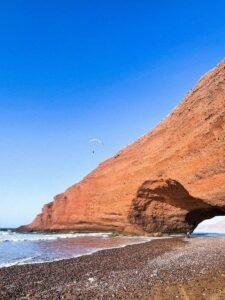 a person flying a kite on a rocky beach.Legzira Beach: