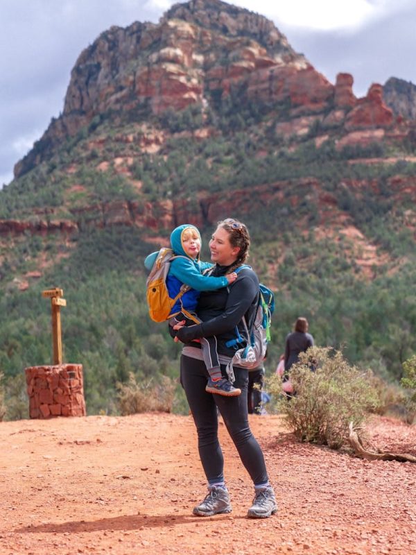 A smiling woman carries her child on a scenic hike in Sedona, Arizona.