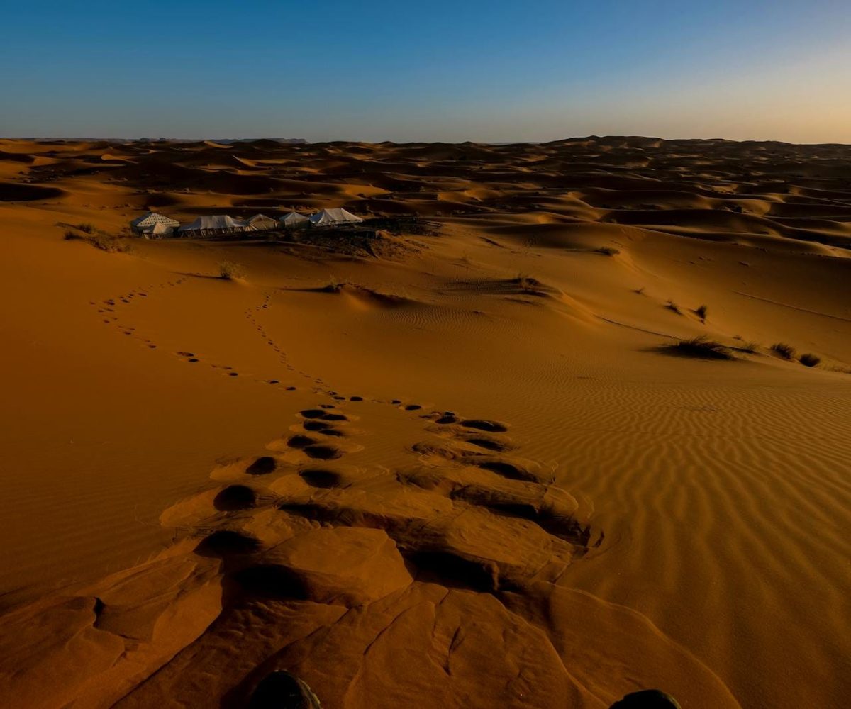 Golden sand dunes and distant tents at sunset in the Moroccan Sahara, Ksar Tanamouste.3 days desert tour from Fes to Marrakech