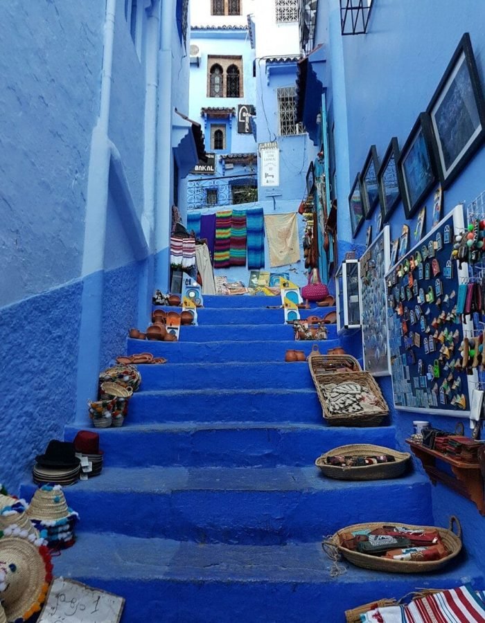 Blue stairs in Chefchaouen lined with woven baskets, hats, and colorful textiles