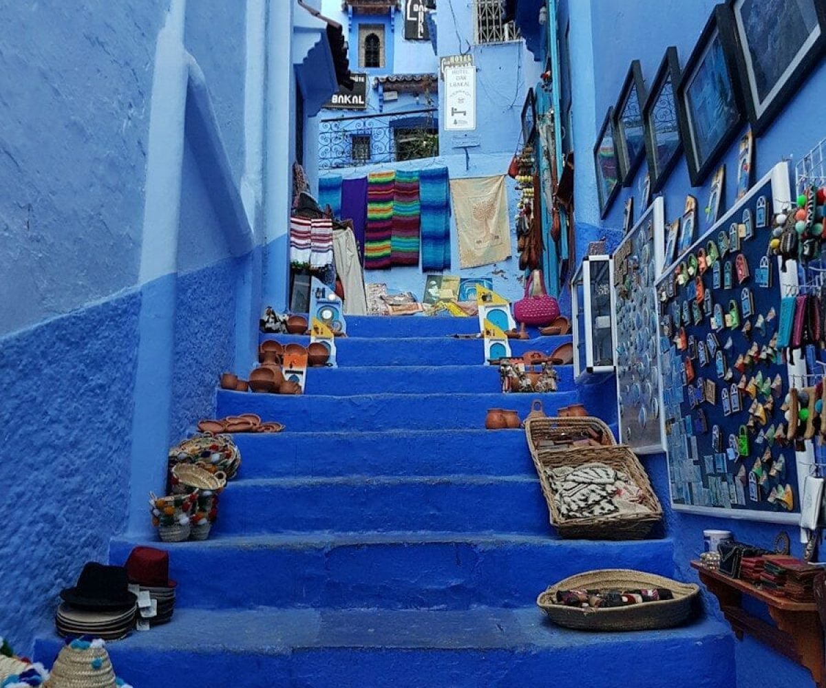 Blue stairs in Chefchaouen lined with woven baskets, hats, and colorful textiles