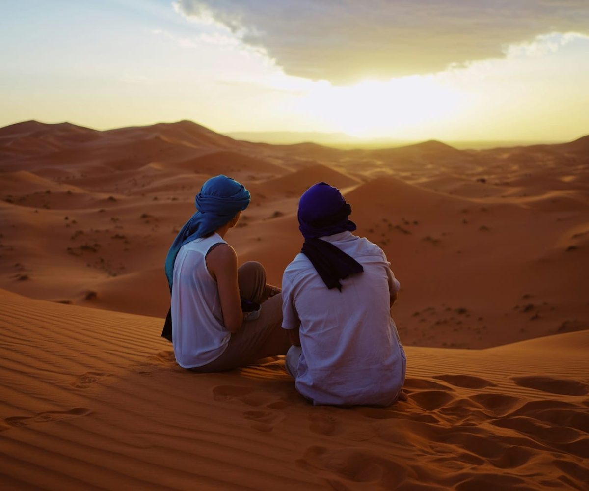 two men sitting on sand dunes,marrakech to merzouga