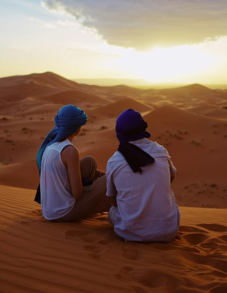 two men sitting on sand dunes